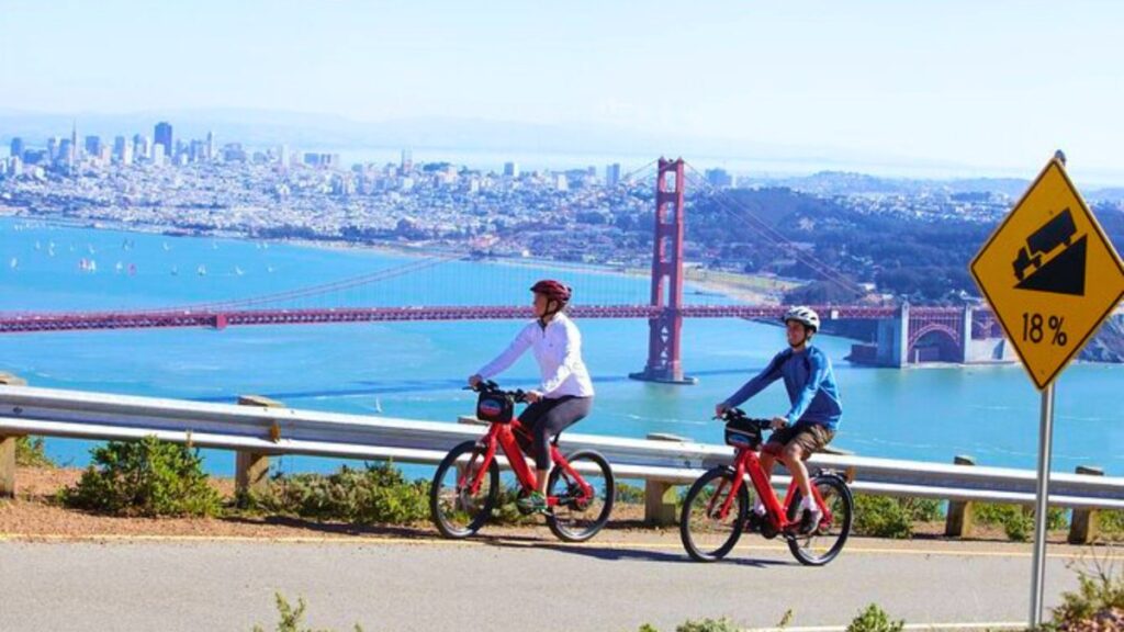 Cyclists riding above the bay with the Golden Gate Bridge behind them